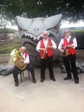 Razzmajazz trio performing with instruments in front of a large mascot sculpture